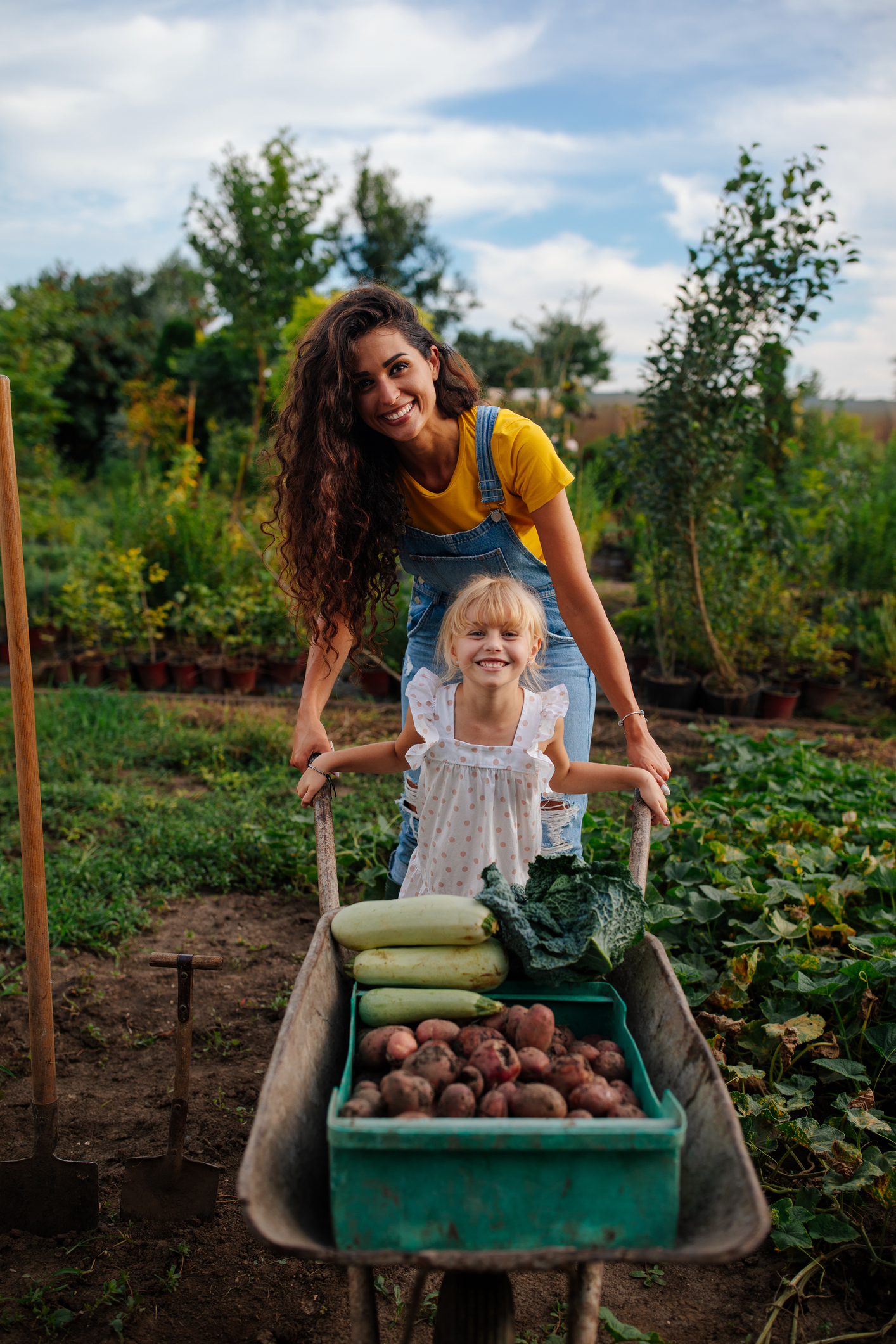 Mother and daughter smiling and holding garden carts filled with vegetables